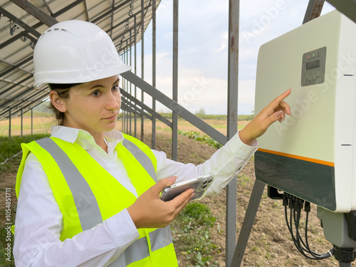 A young woman in a helmet configures a hybrid inverter from the phone. An engineer monitors the operation photo