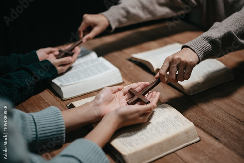 Group of Christians sit together and pray around a wooden table with blurred open Bible pages in their homeroom.