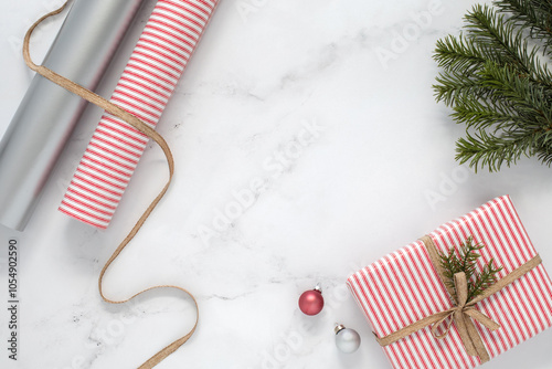 Top down view on a Christmas flatlay on a white marble table top with a copy space. Gift wrap paper, wrapped gift, ribbon, ornaments and a pine branch as a Christmas backdrop