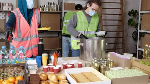 Group of multiracial volunteers in a uniform helping people at charity center. Humanitarian aid concept. Muslim woman and her colleagues working in homeless shelter. Diversity.