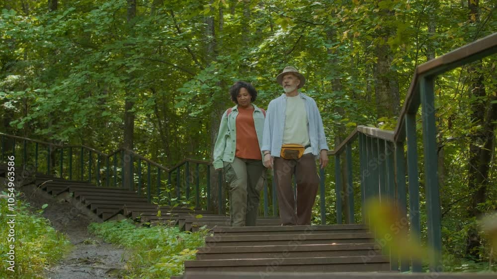 Low angle view of two adult travelers going down wooden stairs while walking in forest Low angle view of two adult travelers going down wooden stairs while walking in forest