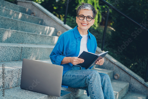 Portrait of pretty aged woman sit stairs hold notepad laptop wear blue shirt weekend walk city center outdoors photo