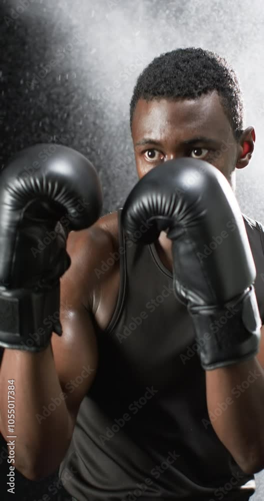 Vertical video: African American male athlete wearing boxing gloves, black background Vertical video: African American male athlete wearing boxing gloves, black background