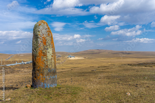 Standing vertical tall stone covered with moss and lichen, Chikiani menhir in sunny weather. Mountains, sky, autumn grass in the background photo