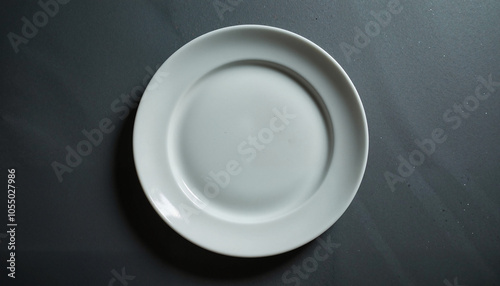 Empty white ceramic plate on dark surface, minimalistic top view