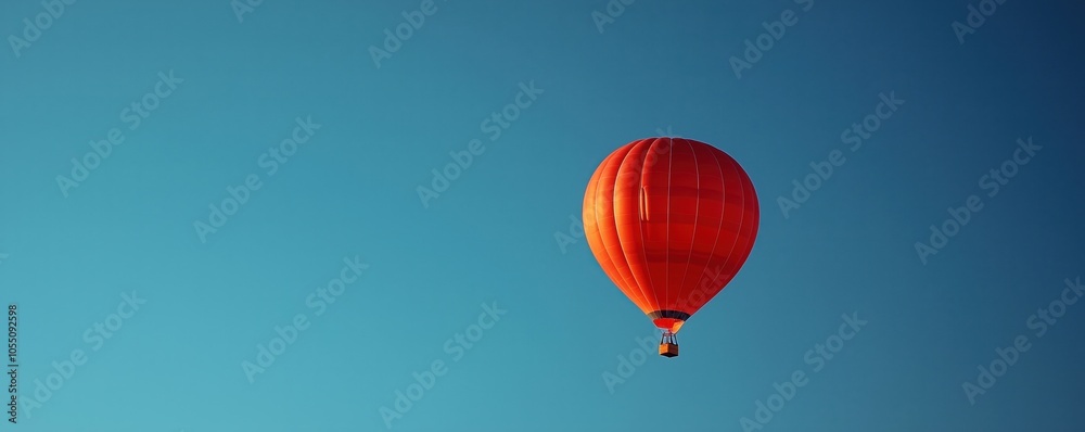 Obraz premium A vibrant red hot air balloon floating against a clear blue sky, evoking a sense of adventure and freedom.
