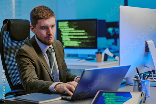 Young Caucasian data security specialist typing on laptop at workplace in modern IT company office