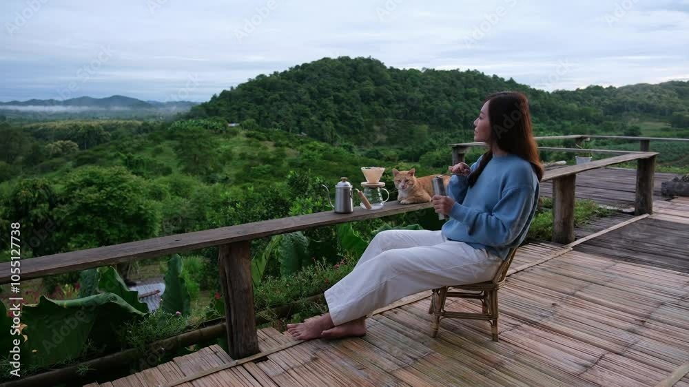A woman grinding coffee while sitting on wooden balcony with a cat and looking at a beautiful mountain view A woman grinding coffee while sitting on wooden balcony with a cat and looking at a beautiful mountain view