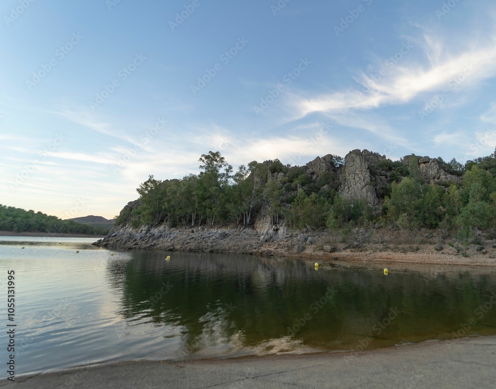 Reservoir surrounded by mountains and green vegetation with clouds reflecting on the water at sunset Reservoir surrounded by mountains and green vegetation with clouds reflecting on the water at sunset