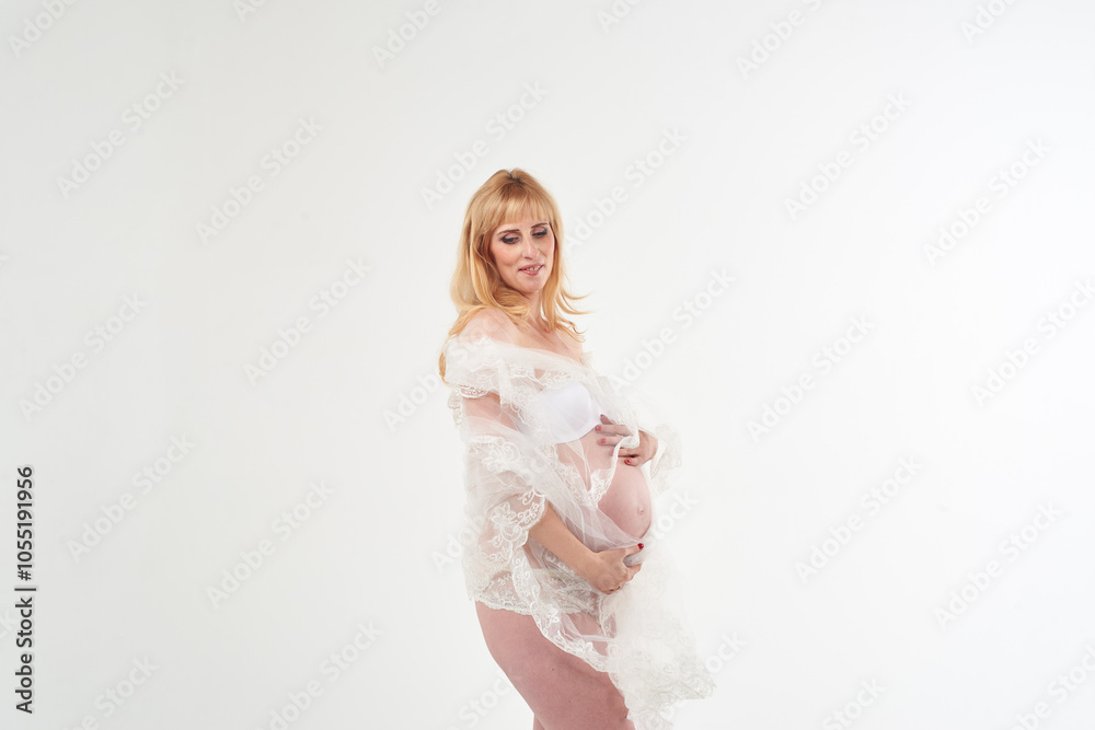 Beautiful pregnant woman in transparent white dress. She has beautiful white panties. She is standing on white background. Happy motherhood. Waiting for a baby. Beautiful pregnant woman in transparent white dress. She has beautiful white panties. She is standing on white background. Happy motherhood. Waiting for a baby.