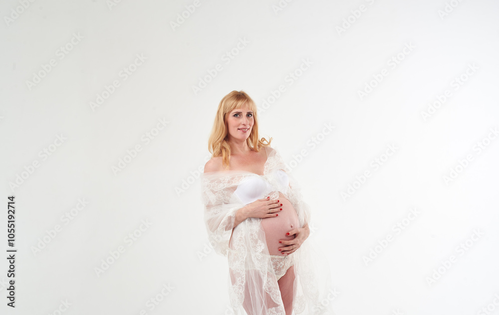 Beautiful pregnant woman in transparent white dress. She has beautiful white panties. She is standing on white background. Happy motherhood. Waiting for a baby. Beautiful pregnant woman in transparent white dress. She has beautiful white panties. She is standing on white background. Happy motherhood. Waiting for a baby.