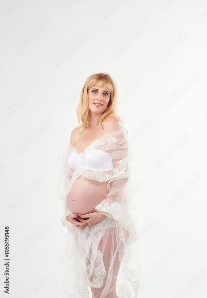 Beautiful pregnant woman in transparent white dress. She has beautiful white panties. She is standing on white background. Happy motherhood. Waiting for a baby. Beautiful pregnant woman in transparent white dress. She has beautiful white panties. She is standing on white background. Happy motherhood. Waiting for a baby.