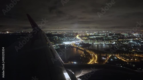 View from cabin of airplane with marker lights flying over night city. Flying a passenger plane low altitude over modern city with rivers and bridge. Business flights between cities Film grain texture