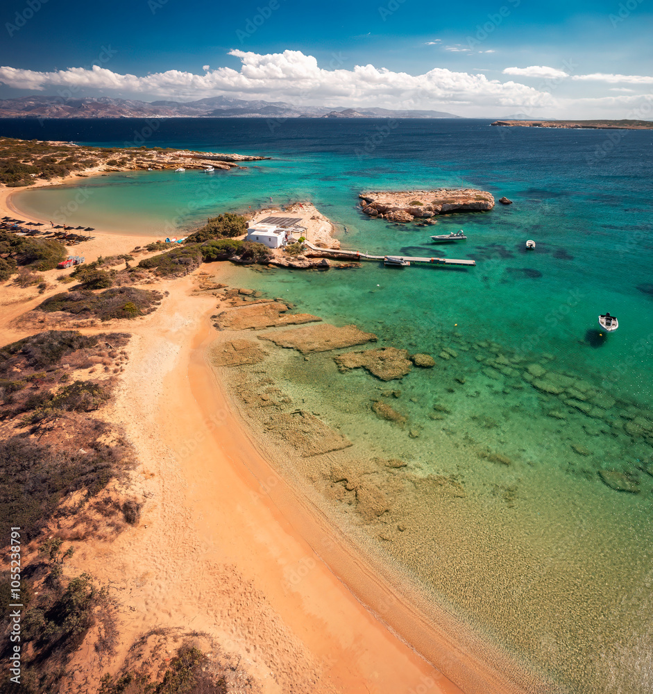 A serene beach on Paros Island, Greece, with golden sands, clear turquoise waters, and gentle waves. Framed by rocky cliffs and lush greenery, it's an idyllic Mediterranean escape under the sun.