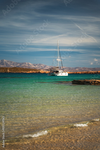 Obraz na płótnie A serene beach on Paros Island, Greece, with golden sands, clear turquoise waters, and gentle waves. Framed by rocky cliffs and lush greenery, it's an idyllic Mediterranean escape under the sun. w salonie