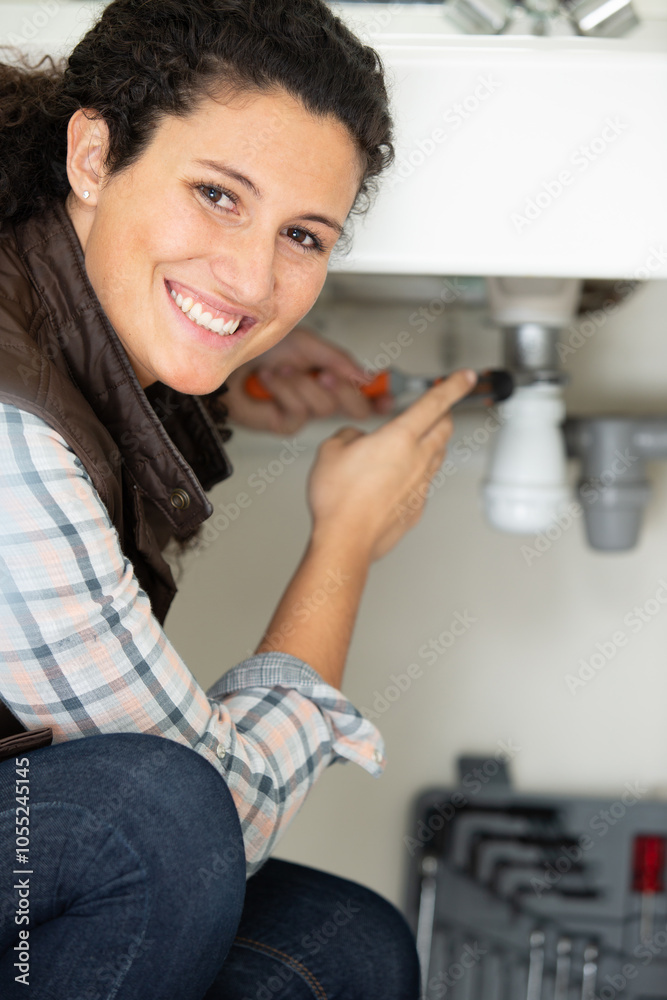 cheerful young woman fixing leaking sink pipe in kitchen