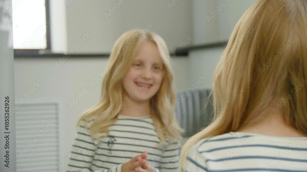 The girl looking at her reflection in the mirror after her first haircut at the hair salon and smiling. A satisfied client. Hair styling. First haircut. The girl looking at her reflection in the mirror after her first haircut at the hair salon and smiling. A satisfied client. Hair styling. First haircut.