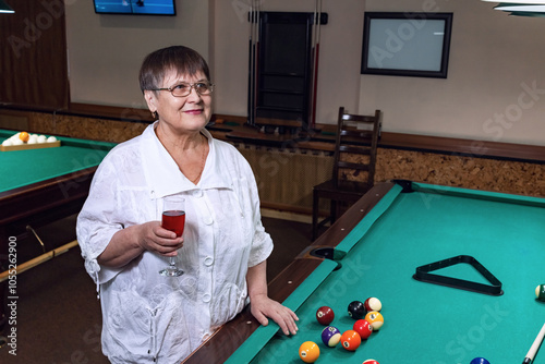 An elderly woman relaxes in a billiard club, drinking wine.