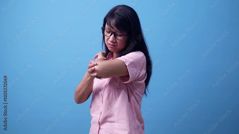 Unhappy sad young Asian woman having pain in his elbow, warming up injured hand after trauma. isolated over blue background Unhappy sad young Asian woman having pain in his elbow, warming up injured hand after trauma. isolated over blue background