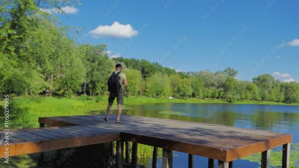 A man stands on a wooden boardwalk in a forest overlooking a river A man stands on a wooden boardwalk in a forest overlooking a river