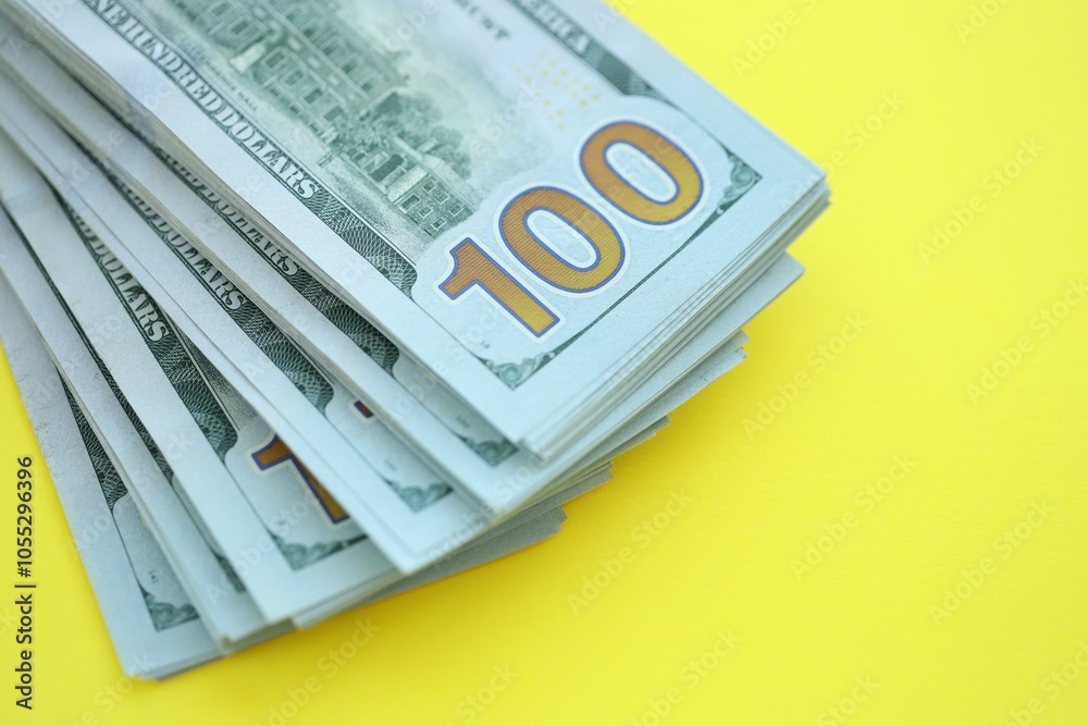 Big amount of hundred dollar bills in thick stack lies on bright yellow color paper background Big amount of hundred dollar bills in thick stack lies on bright yellow color paper background