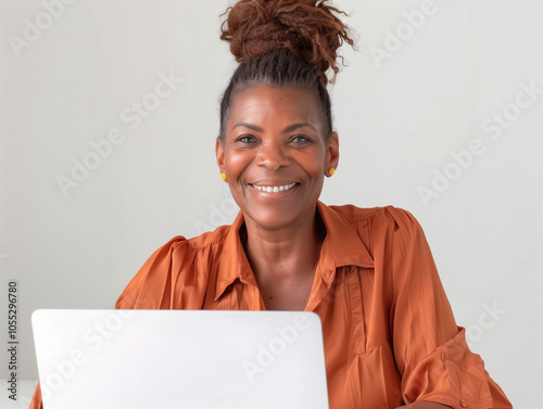 Femme élégante d'origine africaine de 50 à 60 ans en blouse chemise devant un ordinateur sur fond blanc : portrait d'une salariée au travail, sénior et femme dans le monde de l'entreprise