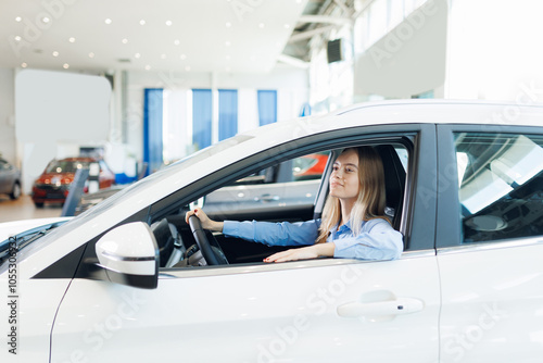 Portrait happy young woman driver behind wheel of new car on test drive before buy in showroom photo