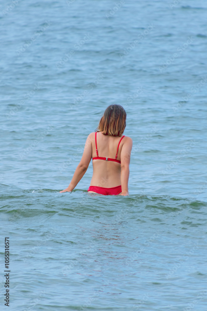 White young woman in a red swimsuit to the waist in the sea. White young woman in a red swimsuit to the waist in the sea.