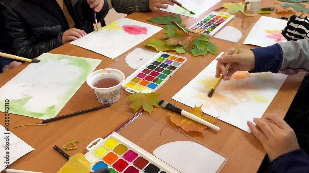 Group of children in the art school studio draw on paper with watercolor paints. Children's hands in the process of drawing
