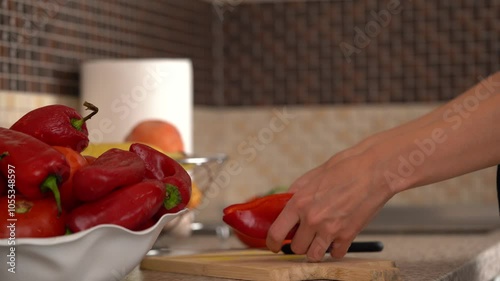 Hands of a young woman are cutting red peppers with a knife on a wooden board for further preparation in the kitchen. The concept of healthy eating, home cooking, a dull knife, sharpening a knife.