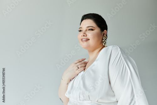 A stunning plus size bride showcases her grace in a white dress and sparkling earrings against a grey backdrop.