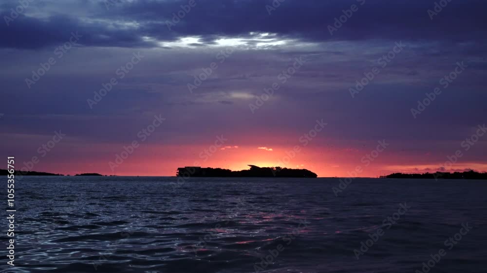 Handshot of intense colors sunset on sea hided island with birds flying above