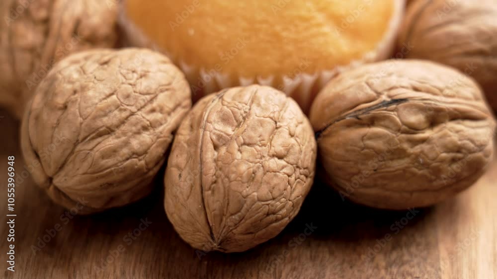 Fresh baked muffin surrounded by raw whole organic walnuts on a wooden surface, showcasing a natural wholesome snack. Close up. Rotation