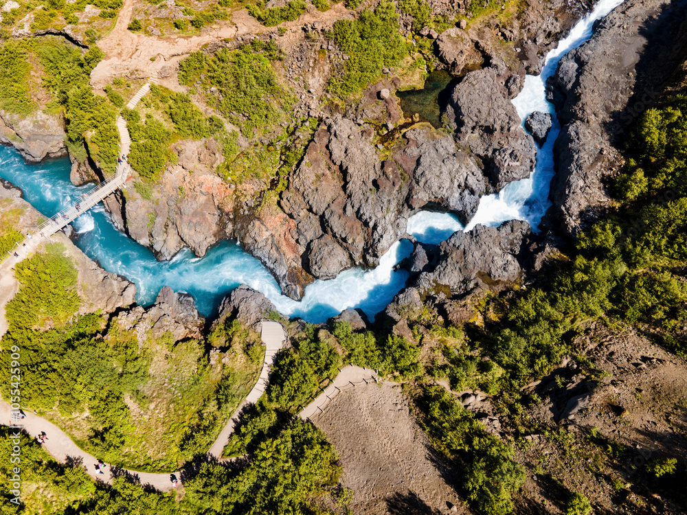Aerial view of the majestic Hraunfossar Waterfall cascading through lush greenery and rocky terrain, Reykholt, Iceland. Aerial view of the majestic Hraunfossar Waterfall cascading through lush greenery and rocky terrain, Reykholt, Iceland.