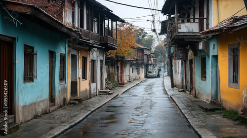 Narrow cobblestone street with colorful old buildings and wooden balconies in a historic town, overcast sky and autumn foliage.