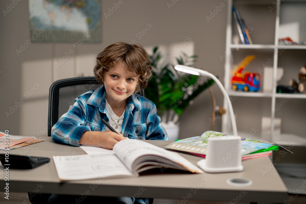 in the children's room a schoolboy in white sweater and a blue checkered shirt at a desk doing homework on his studies writing in a notebook in the children's room a schoolboy in white sweater and a blue checkered shirt at a desk doing homework on his studies writing in a notebook