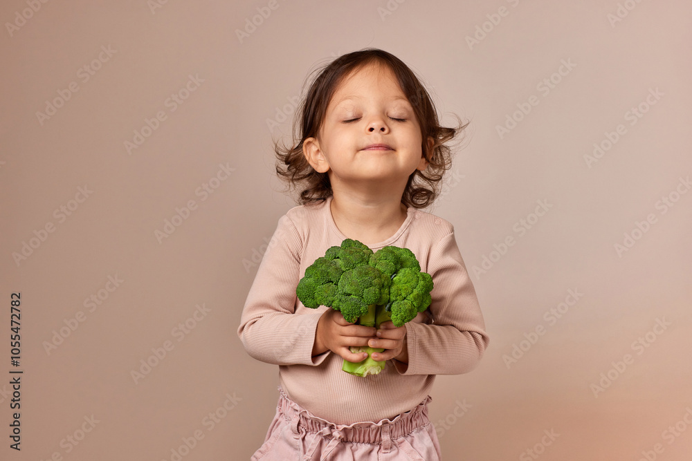 cute little child girl holding fresh green raw broccoli on beige background. healthy baby food. kid loves vegetables cute little child girl holding fresh green raw broccoli on beige background. healthy baby food. kid loves vegetables