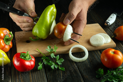 Hands skillfully chop vibrant green peppers, tomatoes, and onions, preparing delicious skewers on a rustic wooden cutting board adorned with fresh parsley