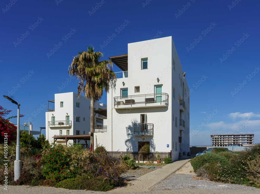 Obraz premium Stunning coastal buildings surrounded by vibrant greenery under a clear blue sky.