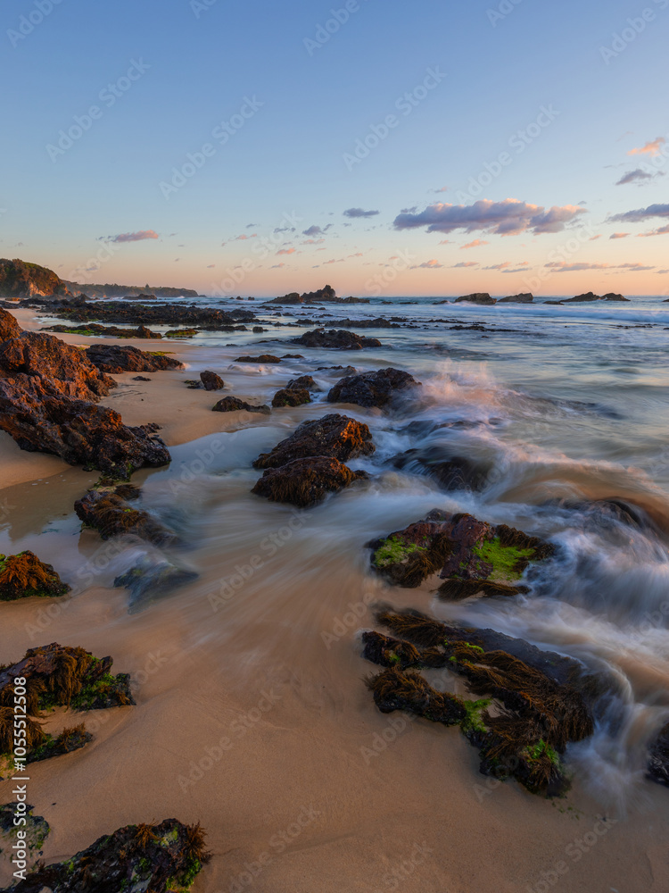Obraz premium Water flows between rocks on the sandy shore.