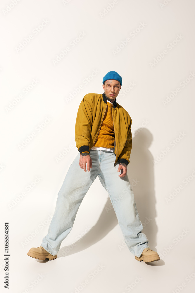 A young man adorned with tattoos showcases a vibrant outfit and confident posture in a studio. A young man adorned with tattoos showcases a vibrant outfit and confident posture in a studio.