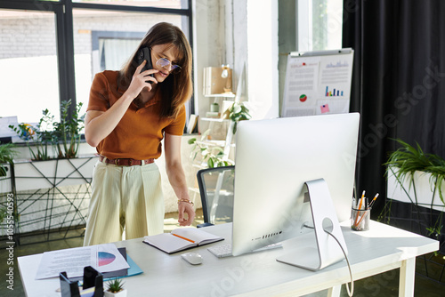 Фотография A young non binary person talks on the phone, focused on their modern office setup