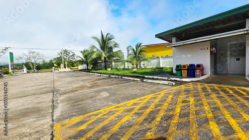 A tranquil scene of a parking lot in a tropical setting, with public restroom, lush greenery, blue sky and Yellow diagonal stripes lines painted on a paved road. Thailand, October 30, 2024   photo