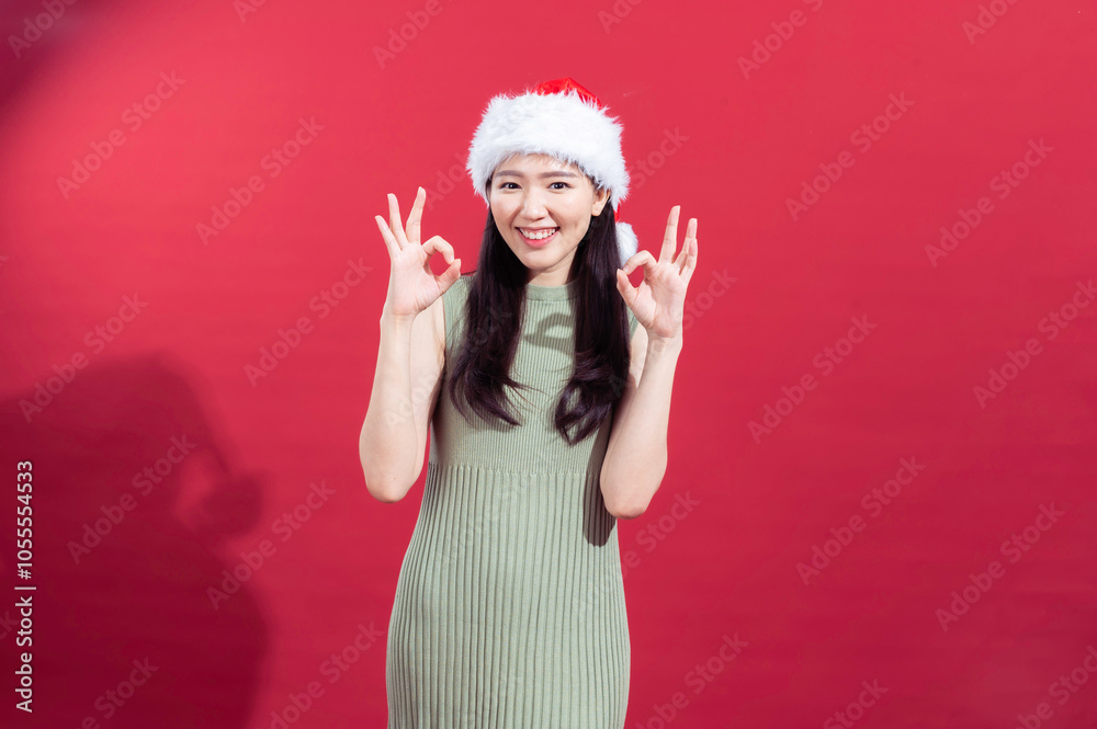 An Asian woman wearing a sleeveless green ribbed dress and a Santa hat is smiling and gesturing the An Asian woman wearing a sleeveless green ribbed dress and a Santa hat is smiling and gesturing the