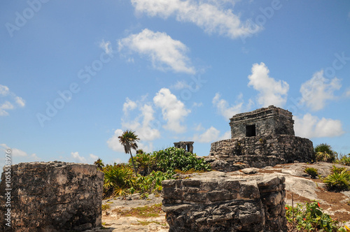 Ancient Tulum ruins under blue sky, surrounded by greenery and rocky landscape.