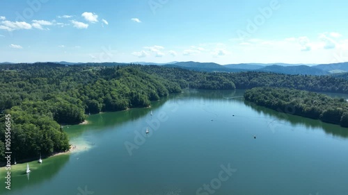 Flying over the lake with a view of the mountains and boats floating on the shore and in the middle of the lake. Beautiful colors of summer. Mavic 3