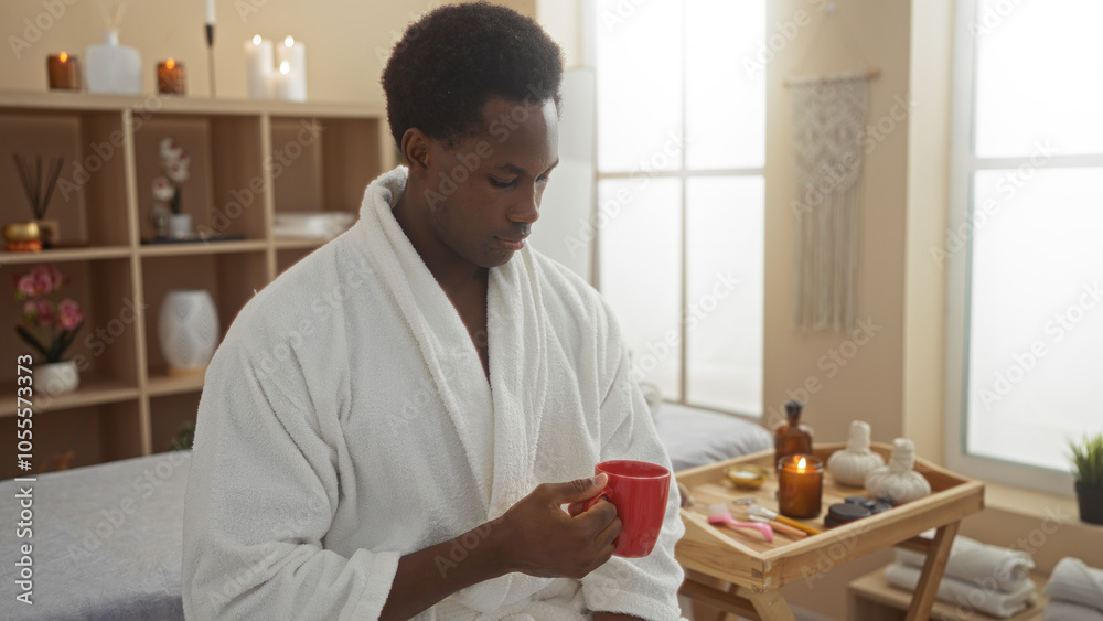 Young man in a white robe enjoying a hot beverage in a peaceful spa room with candles and wellness decor. Young man in a white robe enjoying a hot beverage in a peaceful spa room with candles and wellness decor.