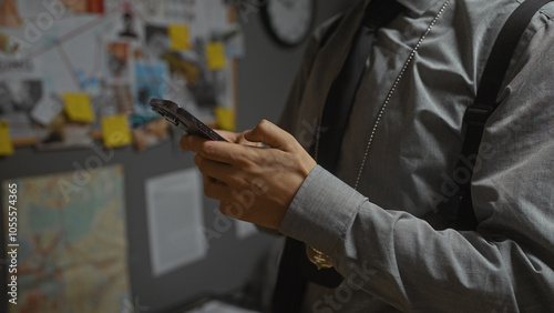 Man in detective's office analyzing evidence board with smartphone, evidencing investigation focus.