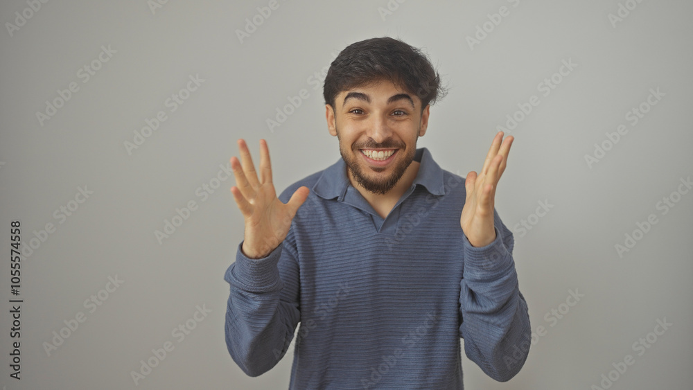 Fototapeta premium Handsome young adult arab man with a beard in casual clothing gestures excitedly against a white background.
