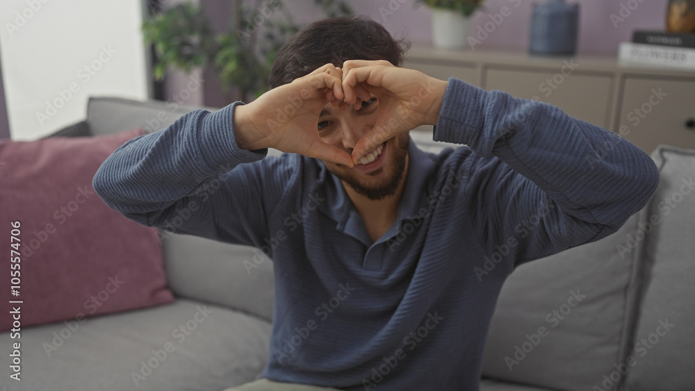 Smiling young man making heart shape with hands in cozy living room Smiling young man making heart shape with hands in cozy living room